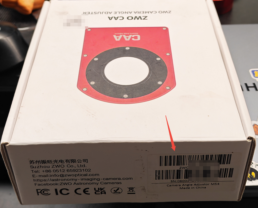 图片展示的是ZWO CA A相机的外包装盒侧面。盒面上方有“ZWO CAMERA ANGLE ADJUSTER”字样，下方是红色的相机安装板图案。盒面左下角有苏州振旺光电有限公司的相关信息，右下角有二维码和“SN:05002”等标识。图片中红色箭头指向二维码右侧的“SN:05002”处，对应文档中“彩色BOX的侧面贴纸中可找到产品SN”的查找设备序列号(SN)方法，直观呈现了SN位置。