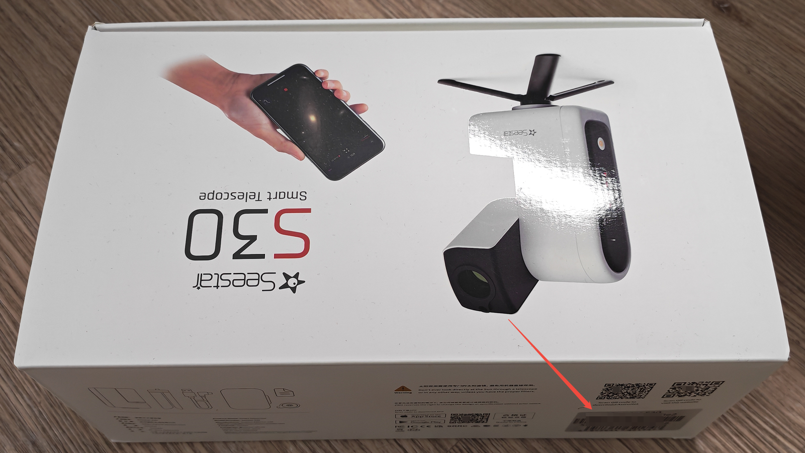 图片展示的是Seestar S30智能望远镜外包装箱侧面。画面中，望远镜的图片位于右上角，下方有红色箭头指向。包装箱侧面有“Seestar”品牌标识及“Smart Telescope S30”字样。该图片与文档中查找设备序列号(SN)的上下文相关，对应查找方法中“外包装箱”步骤，说明在牛皮纸箱侧面的贴纸中可找到产品SN或者WIFI名称后缀，此图直观呈现了外包装箱侧面的位置。